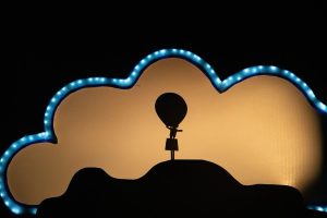 Silhouette of a small hot-air balloon model on a stand in front of a backlit cloud-shaped sign with a blue LED edge.